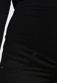 Svarta högmidjade jeans med en slät yta, subtila sömmar och en framficka med en liten metallaccent.