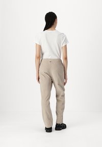 Pantalones de pana beige con un corte relajado y cinturilla elástica. Camiseta blanca con mangas cortas enrolladas. Calzado negro, con detalles mínimos.