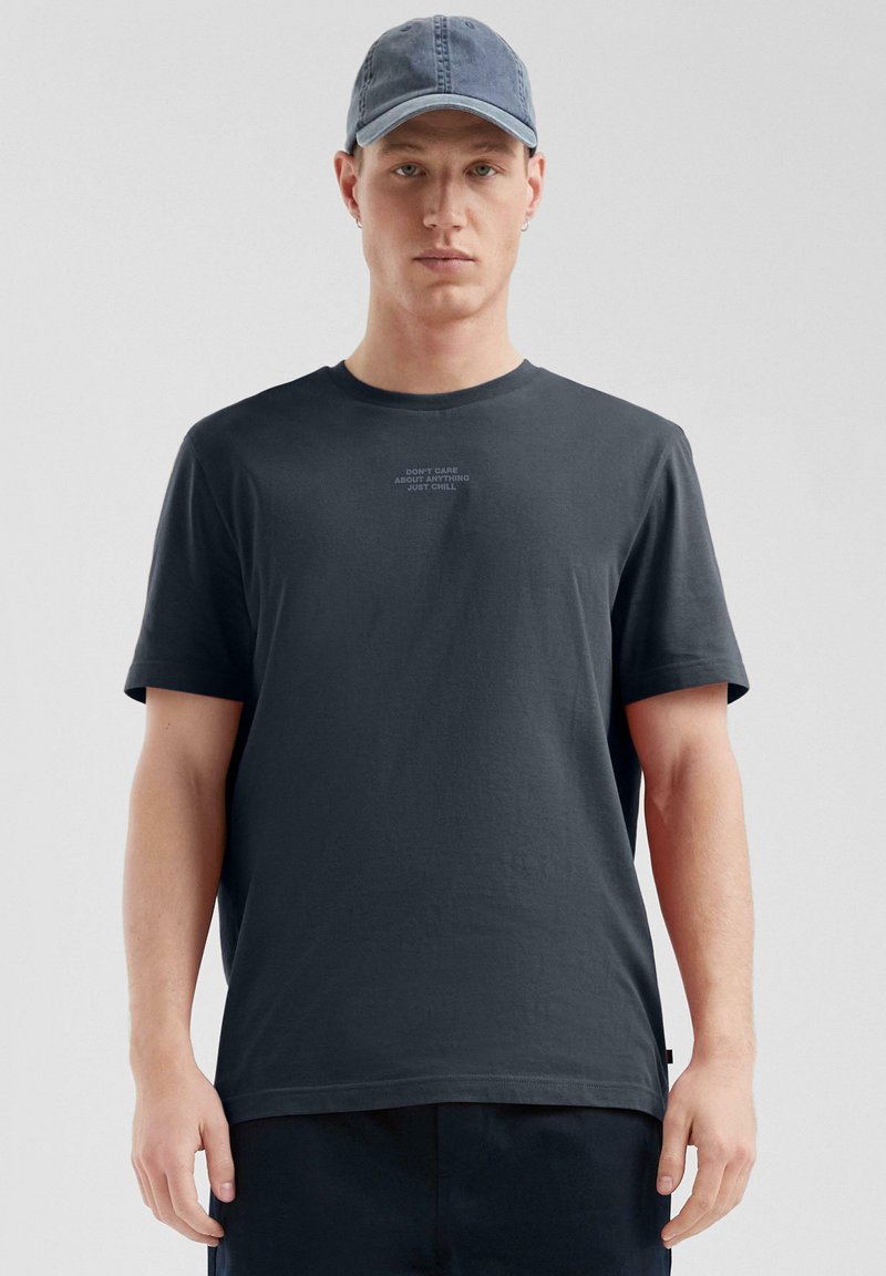 T-shirt en coton gris foncé à manches courtes, avec un texte imprimé dans une couleur plus claire à l'avant. Texture de tissu lisse, coupe décontractée.