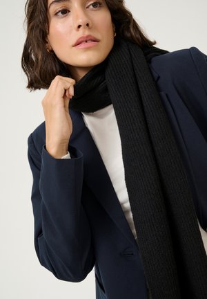 Scarf nero a costine realizzato in morbido tessuto, indossato sopra una maglietta bianca e un blazer blu navy, con un focus ravvicinato sulla texture e sui dettagli.