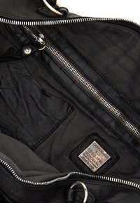 Borsa a mano in pelle nera con cerniere e fodera in tessuto. Etichetta rettangolare evidente all'interno. Texture liscia con un design intricato.