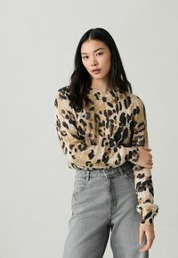Gebreide trui in beige met zwart en bruin luipaardprint, met een brede halslijn en lange mouwen, gecombineerd met grijze high-waisted jeans.
