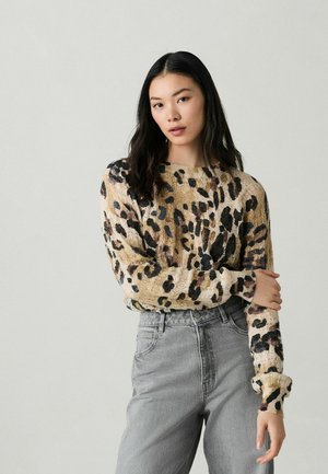 Pull en tricot beige avec un imprimé léopard noir et brun, doté d'une encolure large et de longues manches, associé à un jean gris taille haute.