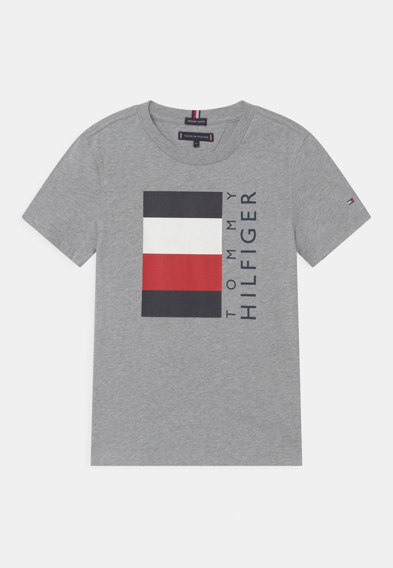Harmaa puuvillapaita, jossa on suorakulmainen graafinen kuvio mustista, valkoisista ja punaisista lohkoista, ja "TOMMY HILFIGER" painettuna sen viereen. Lyhyet hihat.