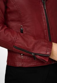 Veste en cuir rouge à la coupe ajustée, dotée de poches zippées, d'accents métalliques et de manches texturées. Fini lisse et forme cintrée.