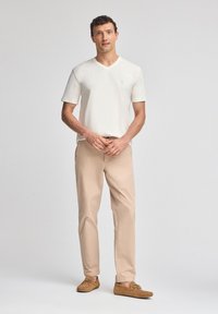 T-shirt bianco a V e pantaloni beige. Tessuto leggero, vestibilità comoda, con mocassini morbidi marroni. Design semplice, dettagli minimi.