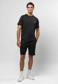 Černé tričko s krátkým rukávem spárované s černými šortkami. Oba kousky mají hladkou texturu a minimalistický design s malým logem na tričku.