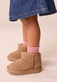 Beige Veloursleder-Stiefeletten mit abgerundetem Zeh und Ziernähten, kombiniert mit hellrosa gerippten Stricksocken, unter einem Jeansrock.