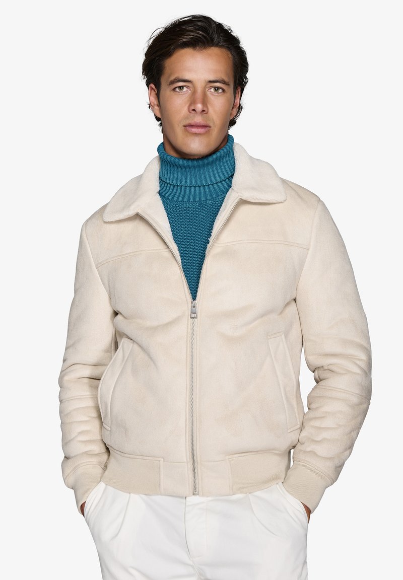 Beige ruskinds bomberjakke med en blød krave, frontlynlås og ribbede manchetter. Bæres over en struktureret teal turtleneck sweater.