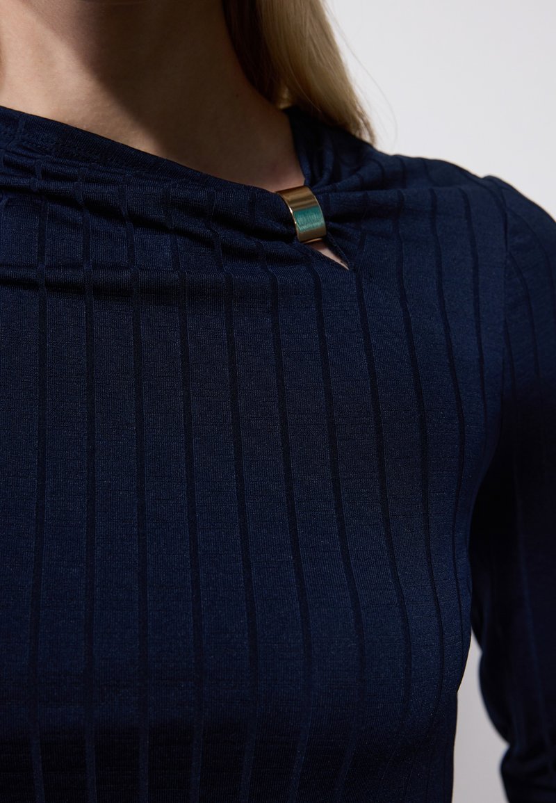 Top a coste navy con scollo a oblò e accenti metallici dorati e teal sul collare, con texture a righe verticali.