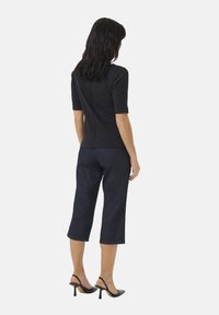 Sort kortærmet top, tætsiddende design, parret med mørkeblå cropped jeans og sorte højhælede sko, set fra ryggen.