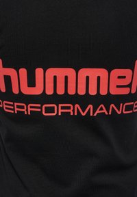 Czarna odzież z wyraźnym czerwonym napisem "hummel PERFORMANCE" na środku materiału.