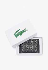 Portafoglio in pelle nera con motivo a losanghe e design in rilievo, custodito in una scatola bianca con un logo di coccodrillo verde.