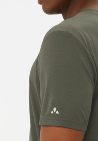 T-shirt olive vert à manches courtes en tissu texturé, avec un petit logo blanc sur la manche gauche. Gros plan de la vue latérale.