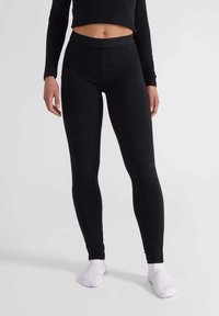Zwarte legging van rekbaar materiaal, met een hoge taille en een gladde textuur. Gecombineerd met witte sokken.