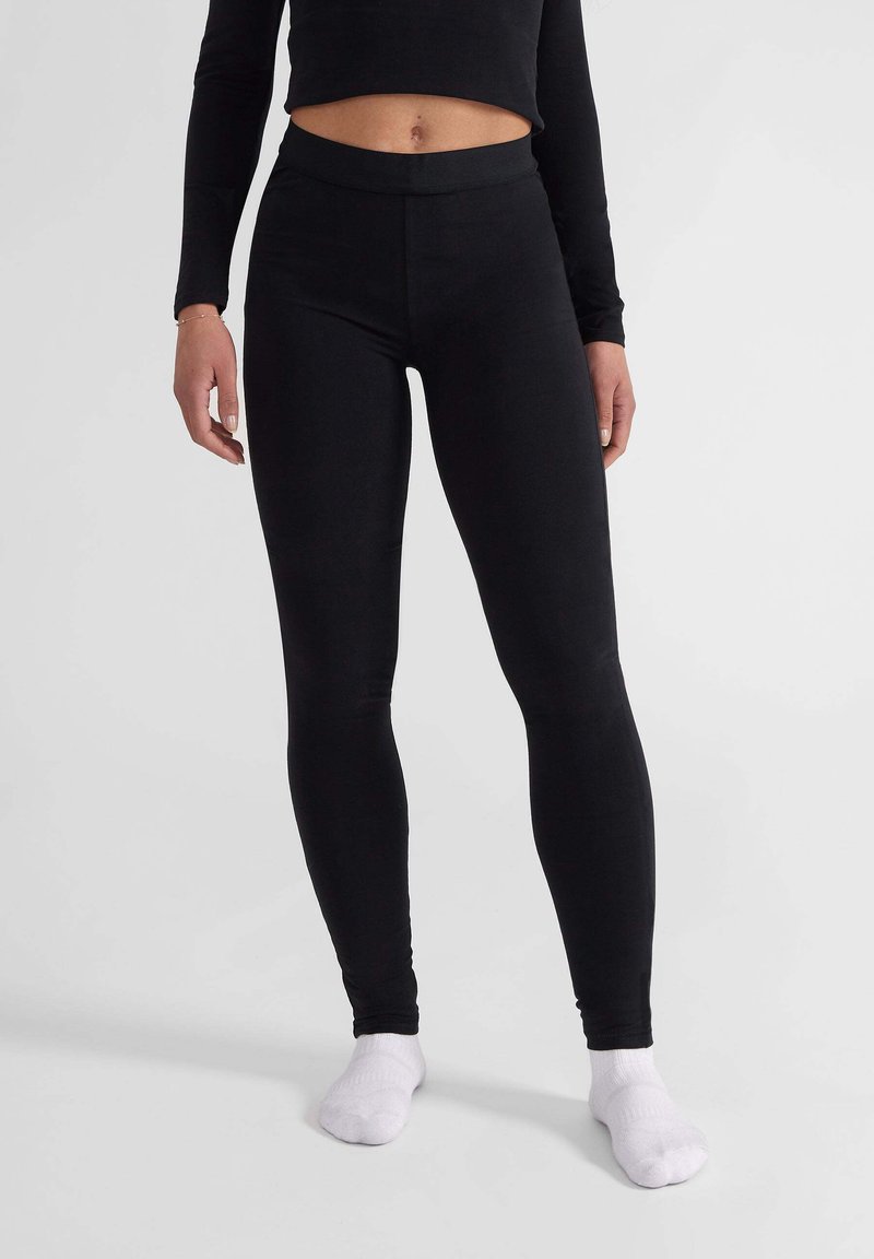 Zwarte legging van rekbaar materiaal, met een hoge taille en een gladde textuur. Gecombineerd met witte sokken.