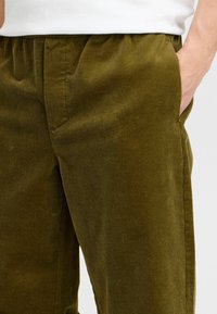 Olive green corduroy pants with a ribbed texture, featuring an elastic waistband and side pockets for practicality.
