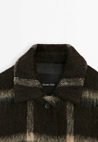 Manteau brun foncé duveteux avec un large col et un seul bouton visible, présentant un motif à carreaux gris clair et beige et une étiquette Massimo Dutti à l'intérieur du col.