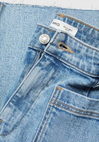Jeans de mezclilla azul claro con cremallera y cierre de botón, con costuras naranjas y un detalle de dobladillo deshilachado y limpio. Etiqueta de la marca visible.