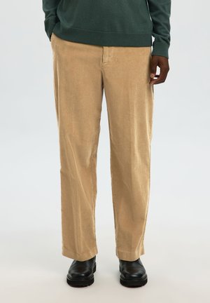 Beige corduroy trousers with a straight-leg cut, featuring vertical ribbing and a front pocket. Paired with black boots.