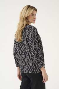 Schwarze Bluse mit einem geometrischen weißen Blättermuster, langärmlig und locker geschnitten. Der Stoff hat eine glatte Textur.