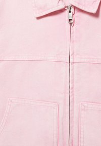 Világos rózsaszín dzseki ezüst cipzárral, gallérral, vízszintes varrással és két elöl lévő, látható varrással díszített téglalap alakú zsebbel.