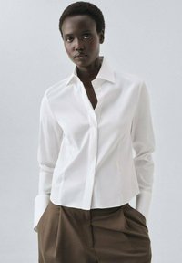 Witte blouse met lange mouwen, voorzien van een knoopsluiting aan de voorkant, een getailleerde pasvorm en een gladde textuur, gecombineerd met een bruin broek.