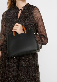 Svart läderhandväska med en strukturerad design, med bruna trähandtag och detaljer i guldton. Slät yta med subtil branding.