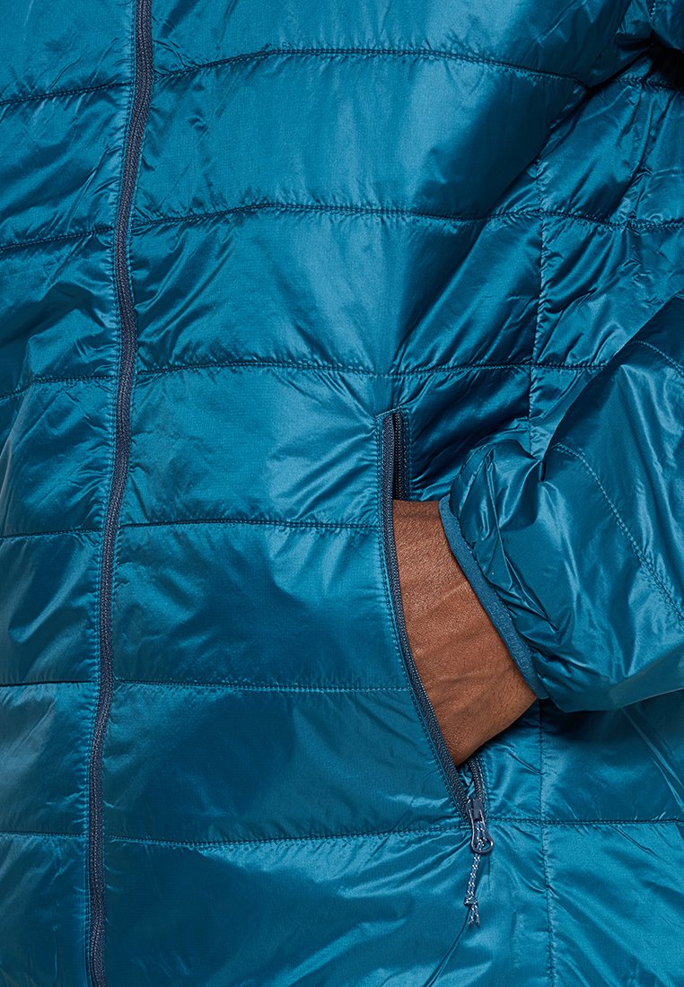 Mano en el bolsillo con cremallera de una chaqueta azul acolchada hecha de un material brillante y aislante.