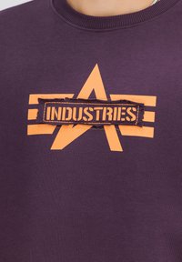 Ljubičasti pamučni dukserica s velikom naran�častom zvijezdom i tekstom "INDUSTRIES" na teksturiranom patcheu, s rebrastim ovratnikom.