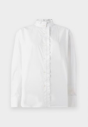 Camisa blanca de botón hecha de algodón. Presenta un alto cuello con volantes y un dobladillo con volantes en el frente. Mangas largas con puños abotonados.