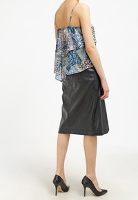 Top sin mangas azul y blanco con patrón y volantes en capas, combinado con una falda de cuero negra hasta la rodilla y zapatos de tacón negros.