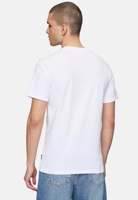 Camiseta de algodón blanca con cuello redondo clásico, mangas cortas y espalda lisa. Combinada con jeans de mezclilla azul claro.