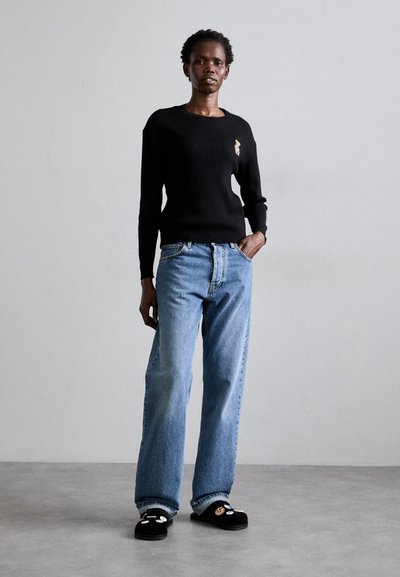 Suéter negro de punto acanalado con un pequeño detalle bordado, combinado con jeans de pierna recta en azul claro y zapatillas negras con adornos.