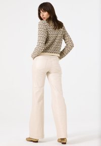 Strickpullover mit einem beigen und schwarzen Muster, kombiniert mit hoch taillierten, hellbeigen ausgestellten Hosen. Textilmaterial und schlichtes Design.