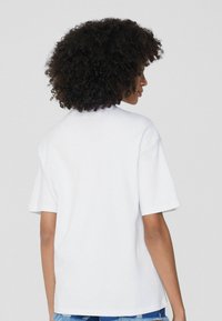 Weißes Kurzarm-T-Shirt mit lockerer Passform, Rundhalsausschnitt und glatter Textur, von hinten betrachtet, ohne sichtbare Logos.