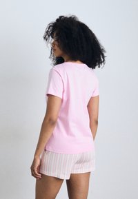 T-shirt em algodão cor-de-rosa combinado com calções claros de riscas. A camisa tem mangas curtas e um decote redondo, enquanto os calções apresentam finas riscas vermelhas.