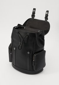 Rucsac din piele neagră cu o suprafață texturată, închidere cu funingine și două buzunare laterale cu fermoar. Interiorul are un căptușeală netedă cu un model.