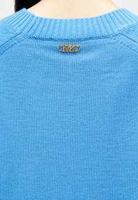 Απαλή μπλε πλεκτή ζακέτα με ραβδωτό λαιμόκοψη, διαθέτει χρυσό κούμπωμα στην πλάτη, δείχνοντας μια λεία, μαλακή υφή.