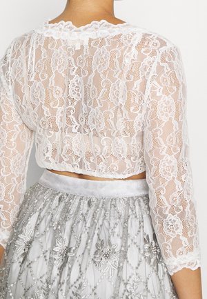 Back view of person wearing a white floral lace cropped top with three-quarter sleeves and a silver skirt embellished with floral patterns.