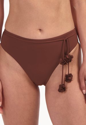 Damski tors w brązowych kąpielówkach z wysokim stanem, ozdobionych wiązaniami po bokach i kwiatowymi detalami z materiału na prawym biodrze.