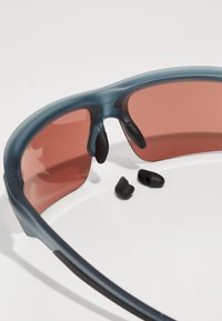 Sportsonnenbrille mit einem blauen transparenten Rahmen und pink getönten Gläsern, ausgestattet mit schwarzen Gummielementen und abnehmbaren Nasenpads.