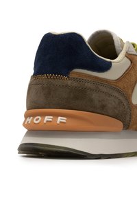 Zapatilla con un cuerpo de ante marrón, acento azul marino, panel beige y un talón naranja con "HOFF" en relieve en blanco. Diseño texturizado y en capas.