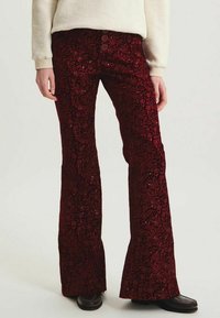 Pantalons rouges évasés en tissu texturé avec un motif floral et des sequins, dotés d'une fermeture à trois boutons à la taille.
