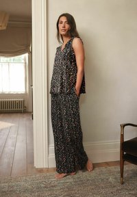 Dvoudílný outfit vyrobený z tmavé tkaniny s květinovým vzorem. Obsahuje tílko bez rukávů a volné kalhoty s kapsami. Hladká textura.
