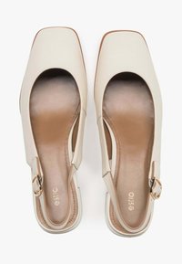 Beżowe skórzane buty typu slingback z kwadratowym noskiem, otwartymi bokami i złotym zapięciem. Teksturowane wkładki z gładką powierzchnią.