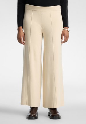 Pantaloni ampi color crema con cuciture davanti, indossati con top nero e stivali massicci marrone scuro, mostrati dalla vita ai piedi.