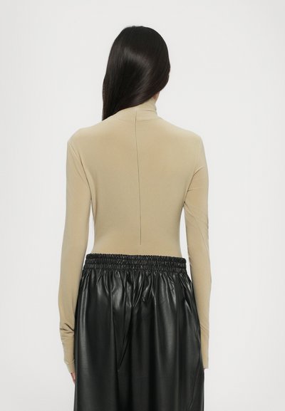 Top beige a maniche lunghe con colletto alto e cucitura posteriore, abbinato a pantaloni in ecopelle neri con vita elastica. Texture complessiva liscia.
