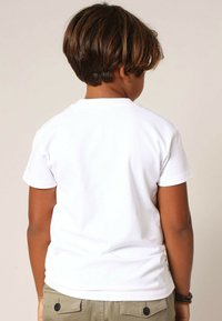 T-shirt blanc à manches courtes avec un col rond, en coton, affiché de dos, associé à un pantalon kaki orné de boutons.