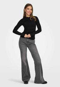 Top negro de manga larga con textura acanalada, combinado con jeans de campana gris claro, ambos ajustados. La modelo está posando con las manos en la cintura.